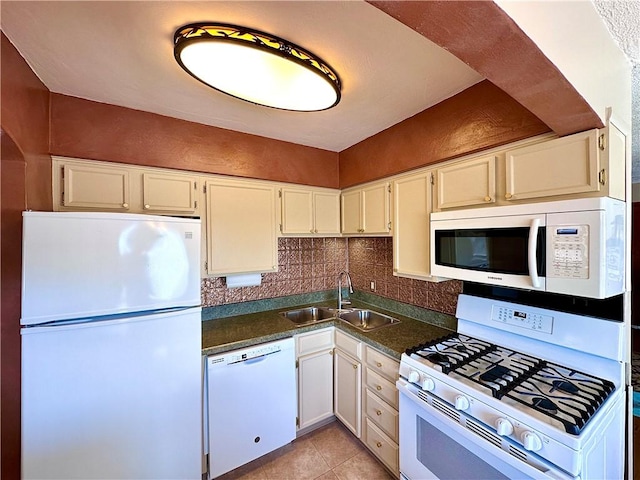 kitchen featuring dark countertops, backsplash, light tile patterned floors, white appliances, and a sink