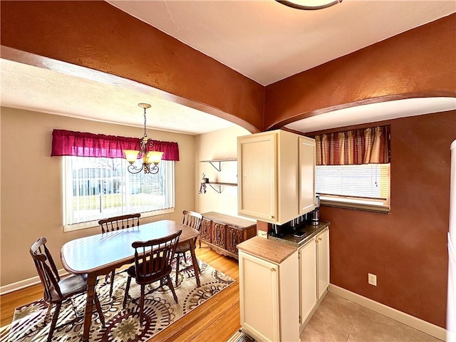 kitchen with baseboards, decorative light fixtures, an inviting chandelier, arched walkways, and white cabinets