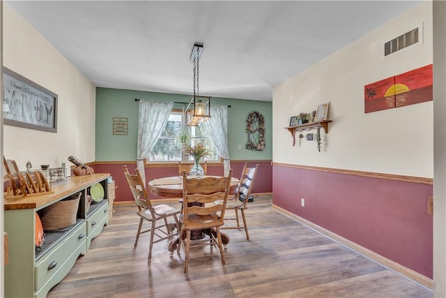 dining space with visible vents, baseboards, wood finished floors, and wainscoting