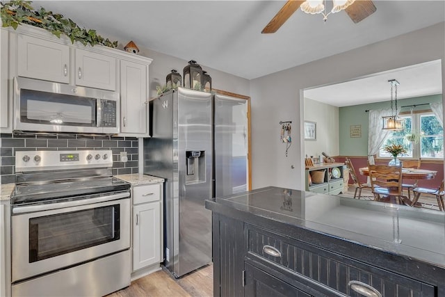 kitchen featuring appliances with stainless steel finishes, white cabinetry, decorative light fixtures, light wood-type flooring, and backsplash