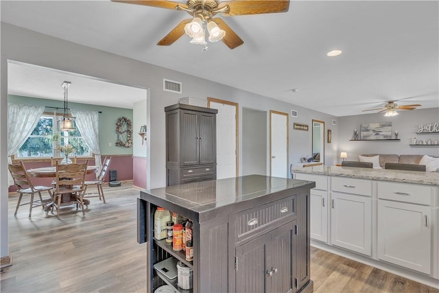 kitchen with visible vents, a kitchen island, ceiling fan, light stone counters, and light wood-style floors