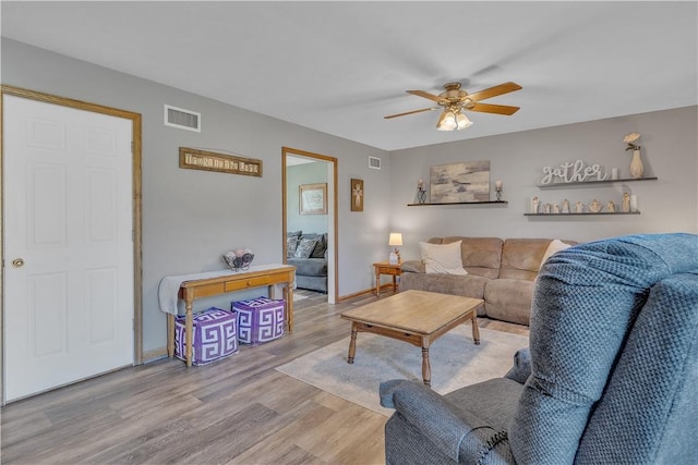 living room with light wood finished floors, visible vents, baseboards, and a ceiling fan