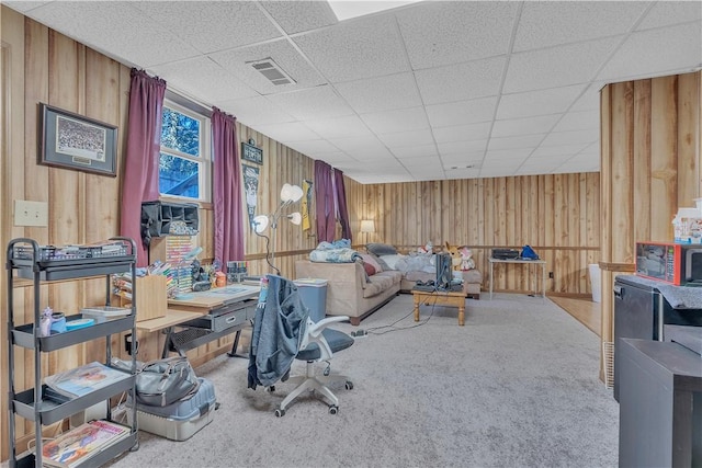 carpeted living room featuring visible vents, a paneled ceiling, and wood walls