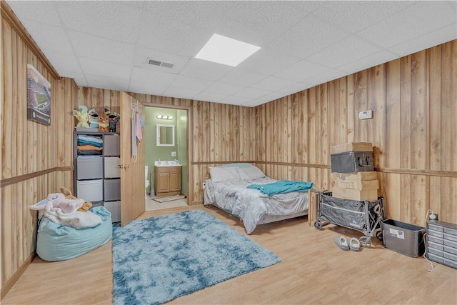 bedroom with visible vents, ensuite bath, wood finished floors, and wood walls