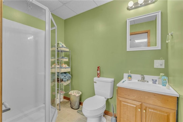 bathroom with a shower stall, baseboards, a drop ceiling, toilet, and vanity