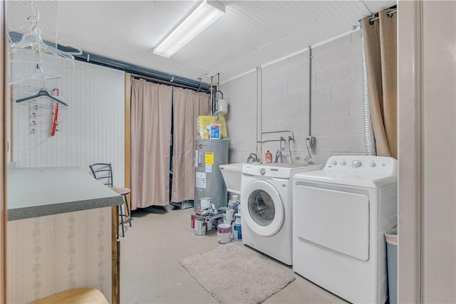 clothes washing area featuring concrete block wall, washing machine and dryer, laundry area, and water heater