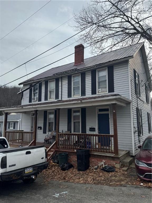 view of front facade featuring covered porch, a chimney, and metal roof