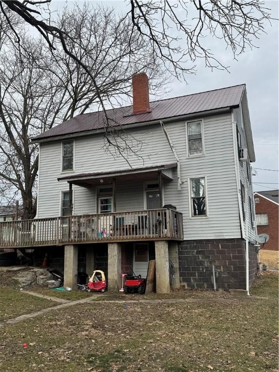 back of property featuring metal roof, a deck, and a chimney