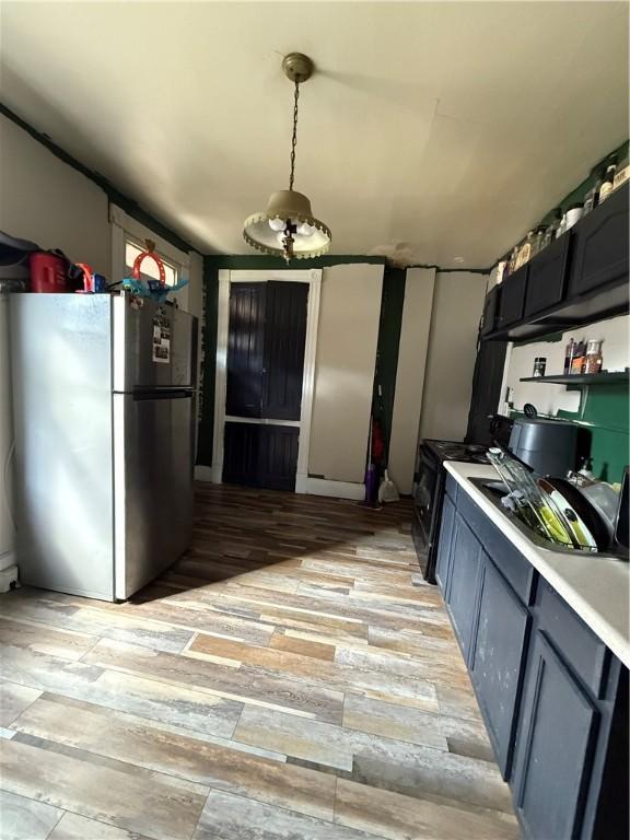 kitchen featuring black gas range oven, light wood-type flooring, light countertops, freestanding refrigerator, and a sink