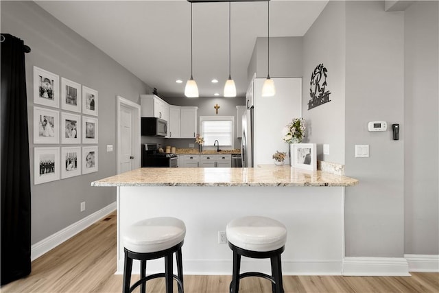 kitchen featuring light stone counters, a peninsula, stainless steel appliances, and a kitchen breakfast bar