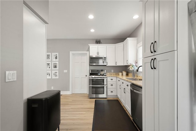 kitchen with a sink, light stone counters, white cabinetry, appliances with stainless steel finishes, and light wood finished floors