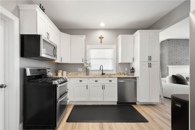 kitchen featuring light stone counters, white cabinetry, stainless steel appliances, and a sink