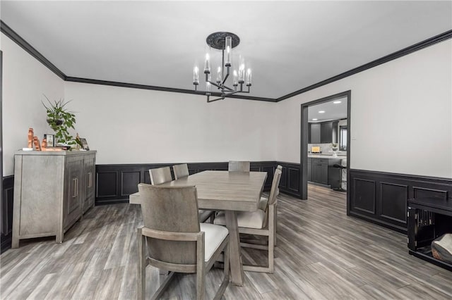 dining space featuring a wainscoted wall, a notable chandelier, ornamental molding, and light wood finished floors