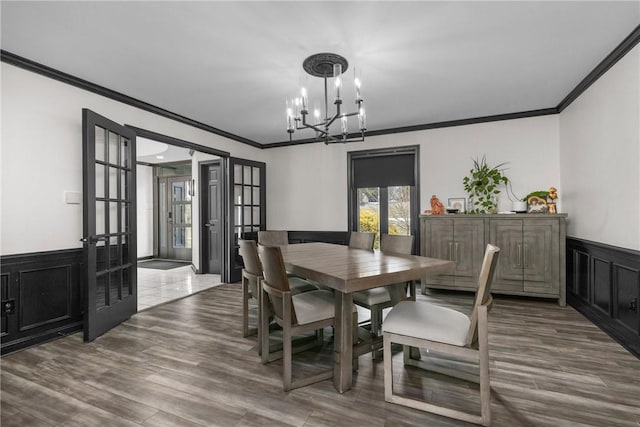 dining space featuring a wainscoted wall, french doors, crown molding, and an inviting chandelier