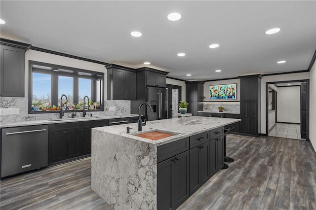 kitchen with a sink, light stone countertops, ornamental molding, stainless steel appliances, and a kitchen island with sink