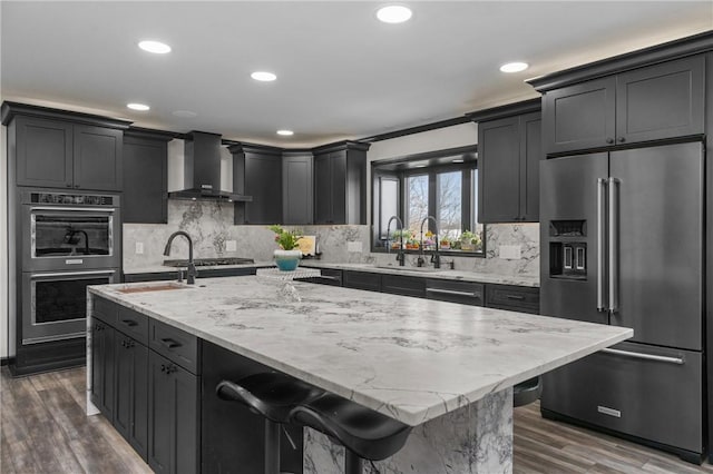 kitchen featuring a sink, stainless steel appliances, dark wood-type flooring, wall chimney exhaust hood, and tasteful backsplash