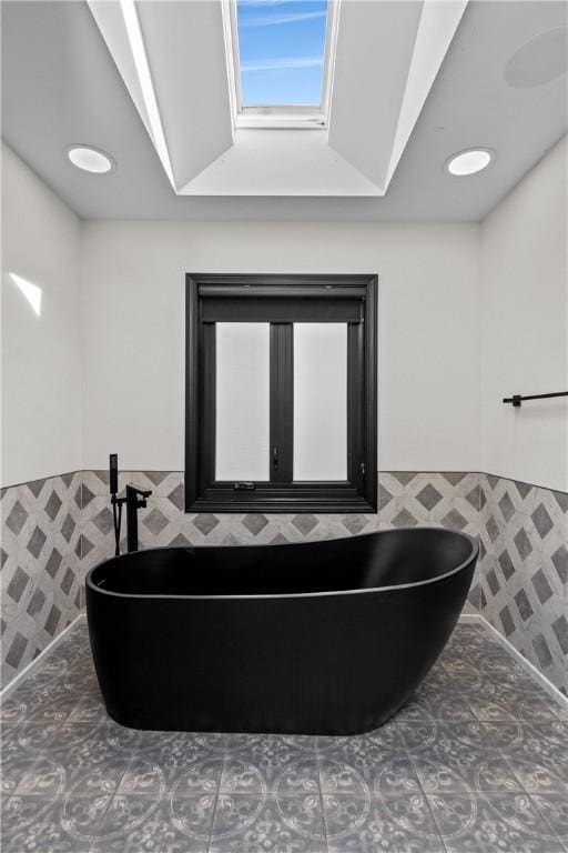 full bath featuring tile patterned floors, a wainscoted wall, a soaking tub, and tile walls