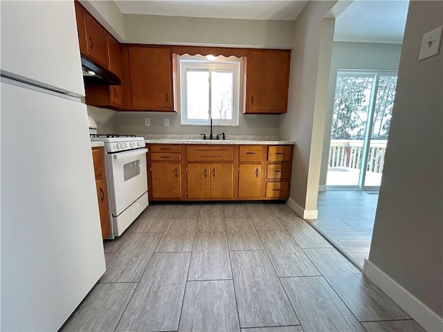 kitchen featuring white appliances, brown cabinetry, a sink, light countertops, and under cabinet range hood