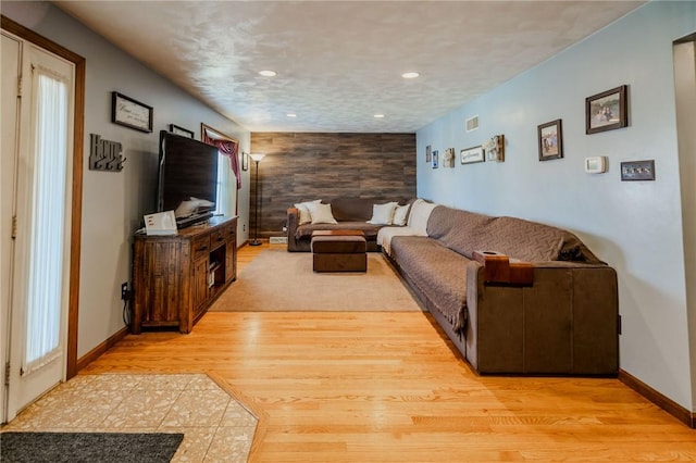 living area featuring recessed lighting, light wood-type flooring, baseboards, and an accent wall