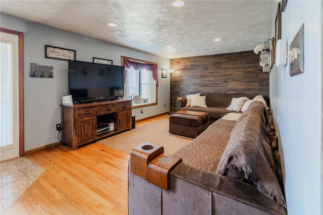 living area with light wood finished floors, wooden walls, an accent wall, baseboards, and recessed lighting