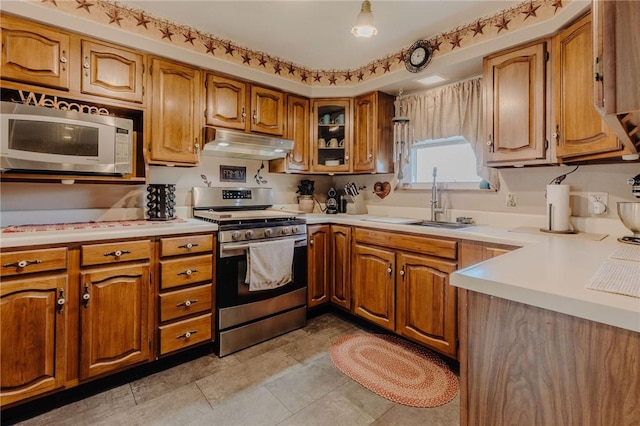 kitchen with under cabinet range hood, a sink, stainless steel appliances, brown cabinetry, and light countertops