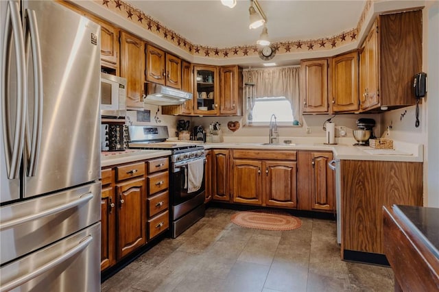 kitchen featuring under cabinet range hood, brown cabinets, stainless steel appliances, and a sink