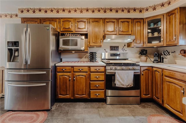 kitchen with under cabinet range hood, light countertops, brown cabinets, and appliances with stainless steel finishes