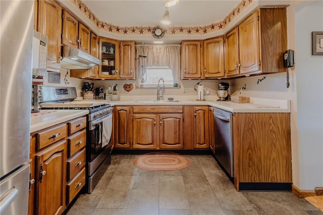 kitchen featuring under cabinet range hood, stainless steel appliances, brown cabinetry, and a sink