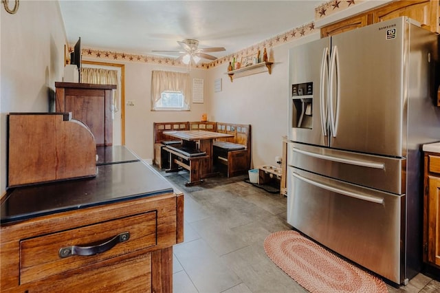 kitchen featuring stainless steel fridge, dark countertops, brown cabinets, and a ceiling fan