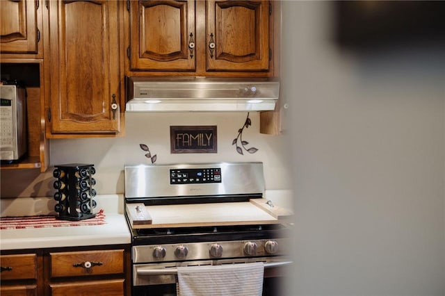 kitchen with ventilation hood, stainless steel gas stove, brown cabinetry, and light countertops