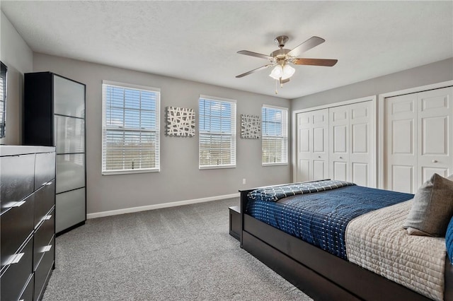 carpeted bedroom featuring a ceiling fan, baseboards, multiple closets, and a textured ceiling