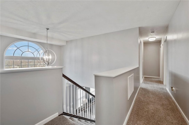 hall with carpet, visible vents, baseboards, an inviting chandelier, and an upstairs landing