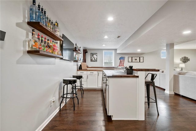 kitchen featuring a kitchen breakfast bar, dark wood-style floors, open floor plan, a peninsula, and white cabinets