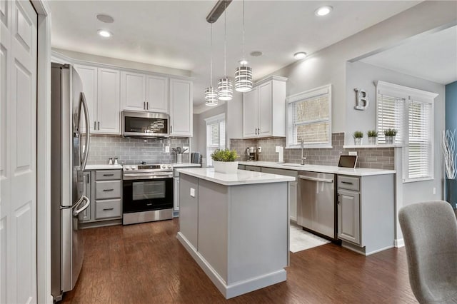 kitchen with gray cabinetry, a kitchen island, dark wood-style floors, appliances with stainless steel finishes, and light countertops