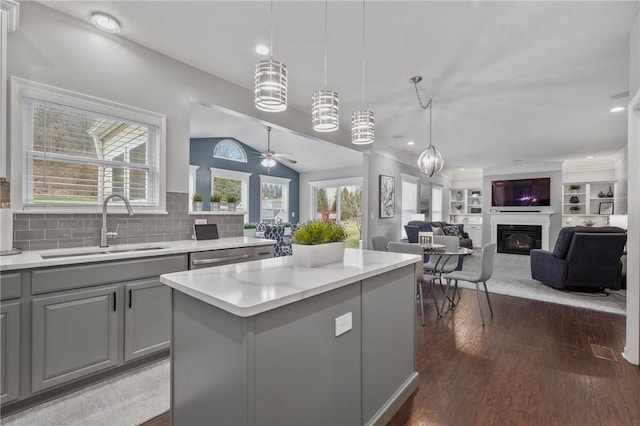 kitchen with gray cabinetry, a center island, dark wood finished floors, a glass covered fireplace, and a sink