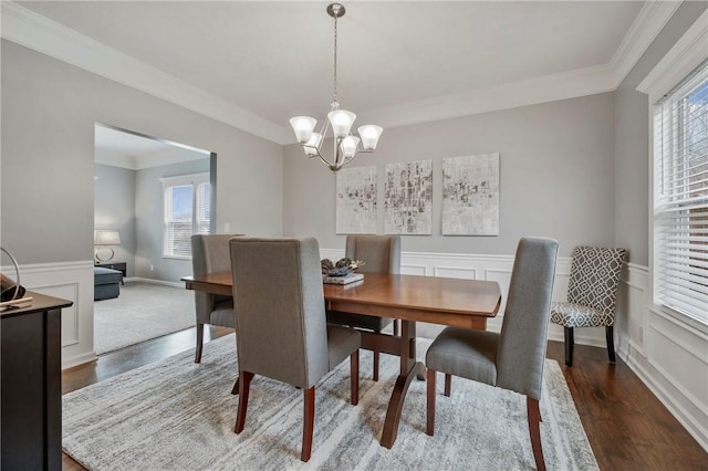 dining area featuring ornamental molding, wainscoting, an inviting chandelier, wood finished floors, and a decorative wall