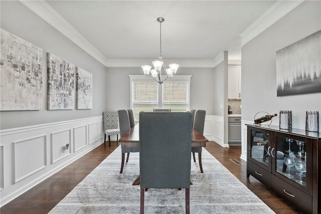 dining room featuring ornamental molding, dark wood-style floors, an inviting chandelier, wainscoting, and a decorative wall