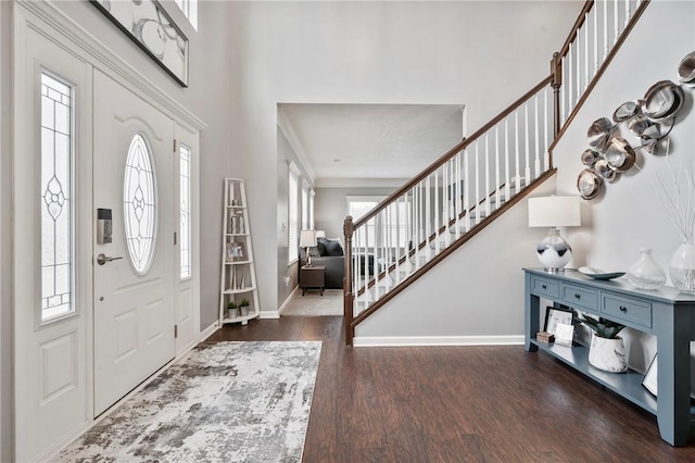 entryway featuring crown molding, baseboards, stairs, a towering ceiling, and wood finished floors