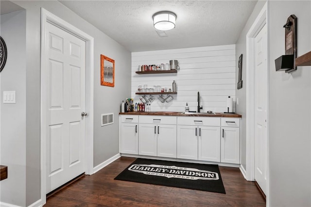 bar featuring visible vents, dark wood finished floors, a sink, indoor wet bar, and a textured ceiling