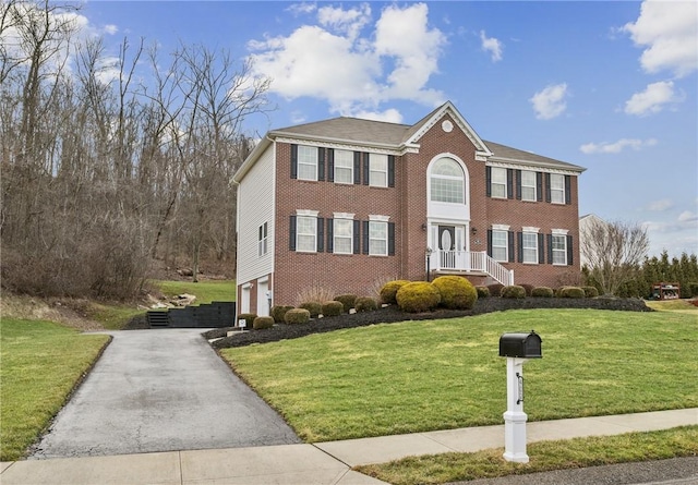 view of front of house featuring aphalt driveway, brick siding, an attached garage, and a front lawn