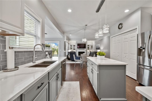 kitchen featuring a fireplace, dark wood-style flooring, a sink, stainless steel appliances, and backsplash