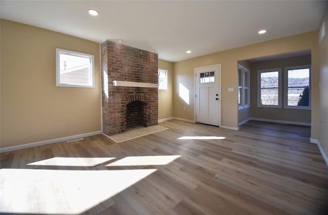 unfurnished living room with recessed lighting, a brick fireplace, baseboards, and wood finished floors