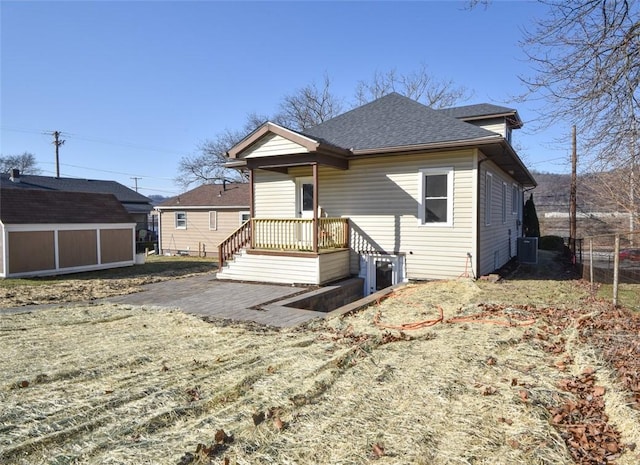 rear view of property featuring central air condition unit, an outdoor structure, roof with shingles, and fence