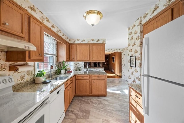 kitchen featuring a sink, white appliances, brown cabinetry, and wallpapered walls