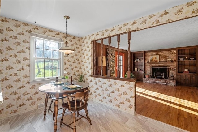 dining space featuring wallpapered walls, wood finished floors, a fireplace, and baseboards