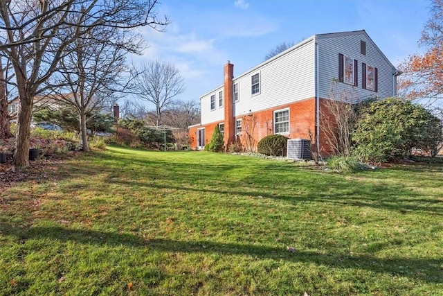 view of side of home featuring brick siding, a chimney, and a lawn