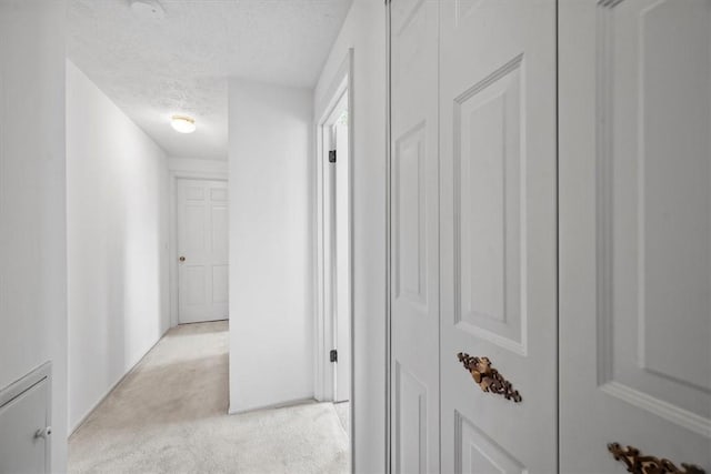 corridor with light colored carpet and a textured ceiling