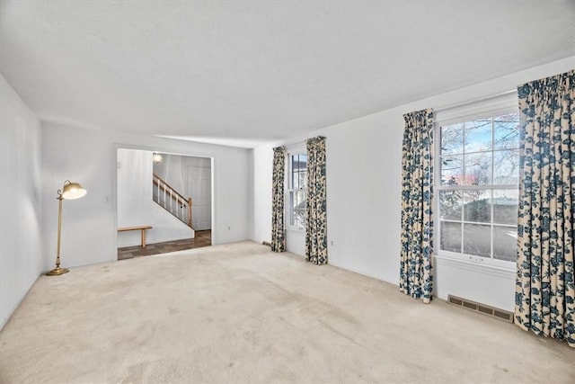 empty room with a wealth of natural light, visible vents, carpet flooring, and stairway