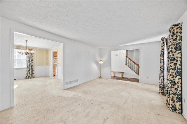 unfurnished living room with a notable chandelier, visible vents, stairway, and carpet