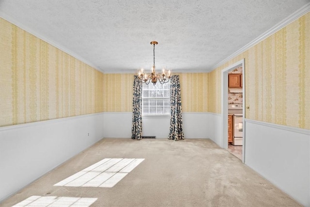 empty room with carpet floors, wallpapered walls, a textured ceiling, crown molding, and a chandelier